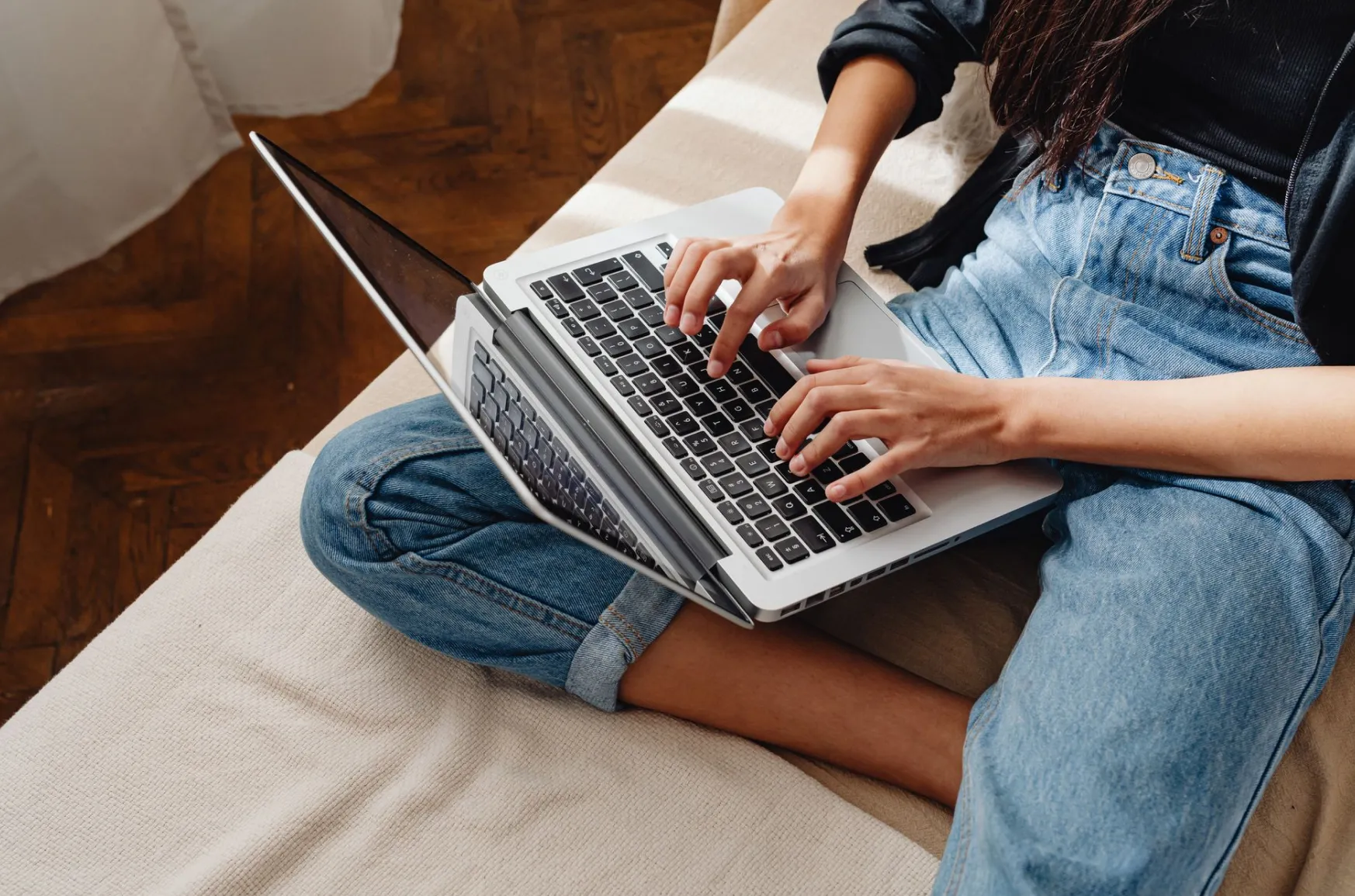 Young woman working on a laptop at home, sitting on a couch, during the day.